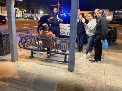 Volunteers and Glendale Police Officers contact a homeless individual sitting on a bus bench during the evening portion of the 2026 Glendale Homeless Count.
