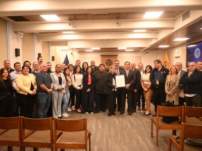 A large group of people smile for a photo with the building safety proclamation in Glendale City Counil Dias